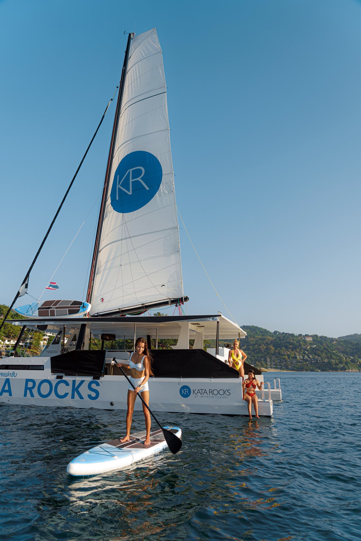 a person is standing on a paddle board in front of a catamaran in Nui Beach Phuket